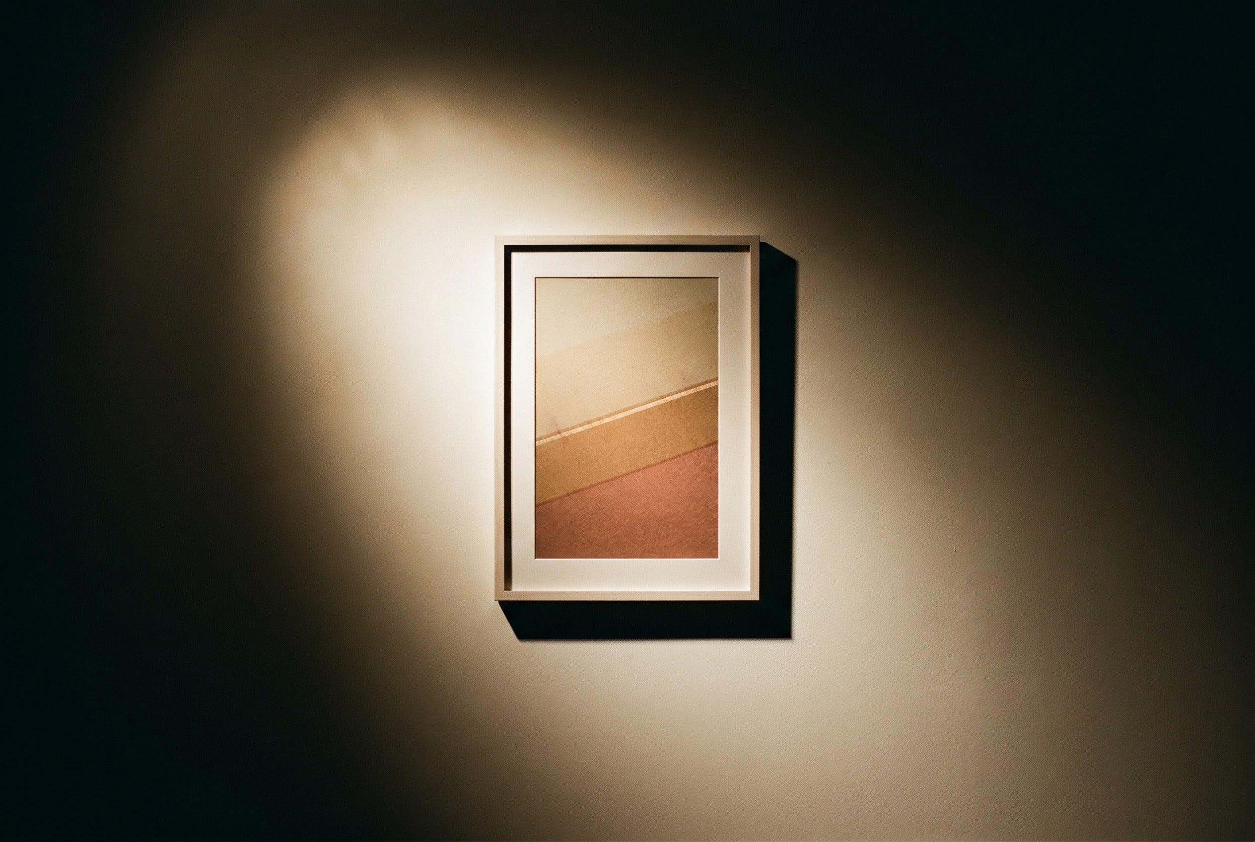 A framed print washed by a warm picture light at an angle